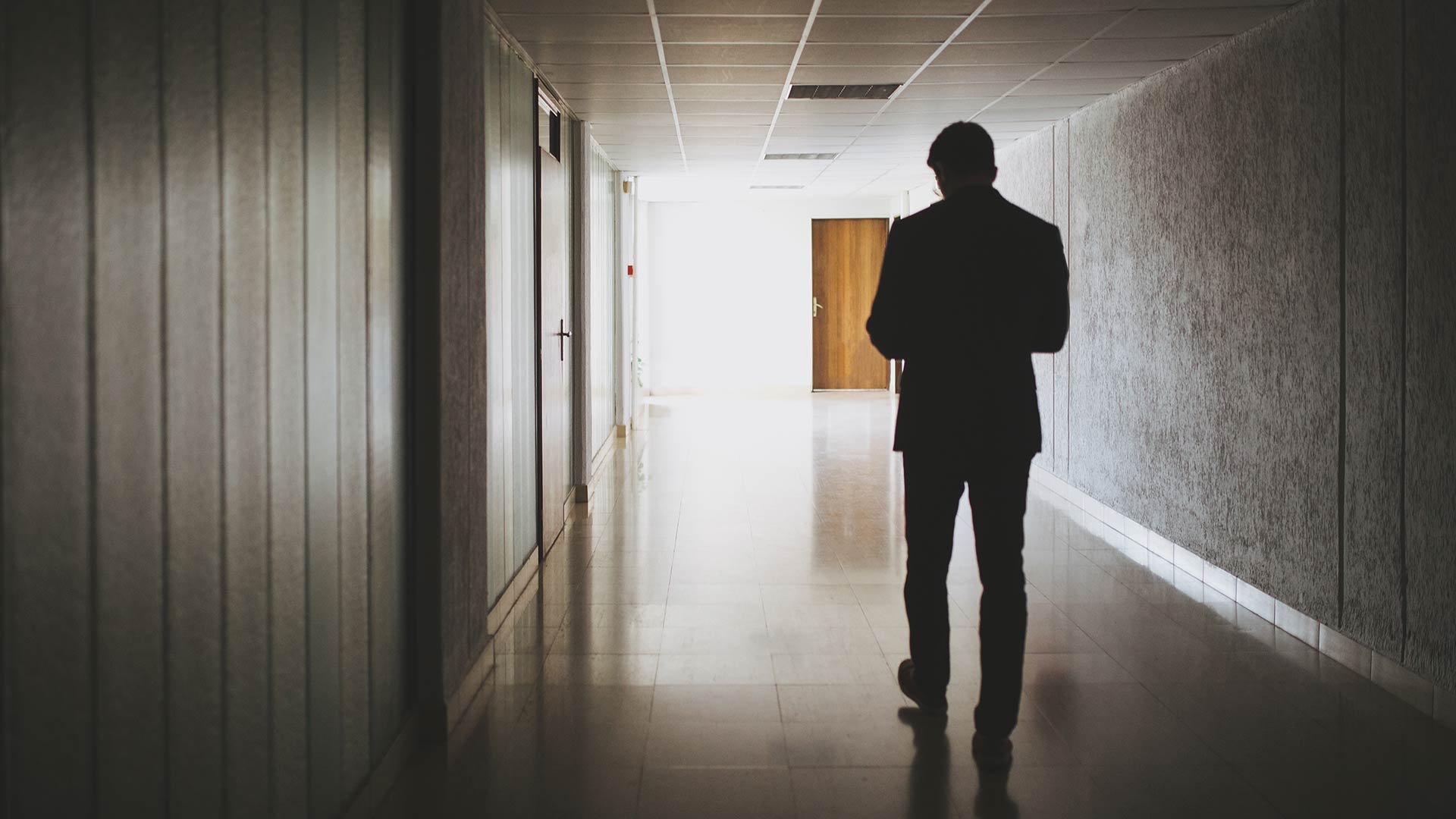 Silhouette of a man walking down a hallway looking at a mobile device