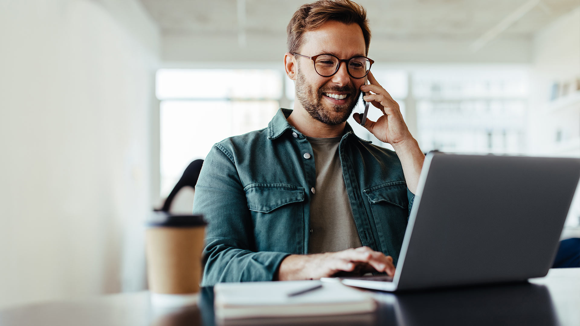 Man talking on a phone while in front of a laptop